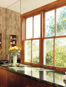 Pella Designer Series wood window installed above kitchen sink, featuring large glass panes, natural wood interior finish, and energy efficient design